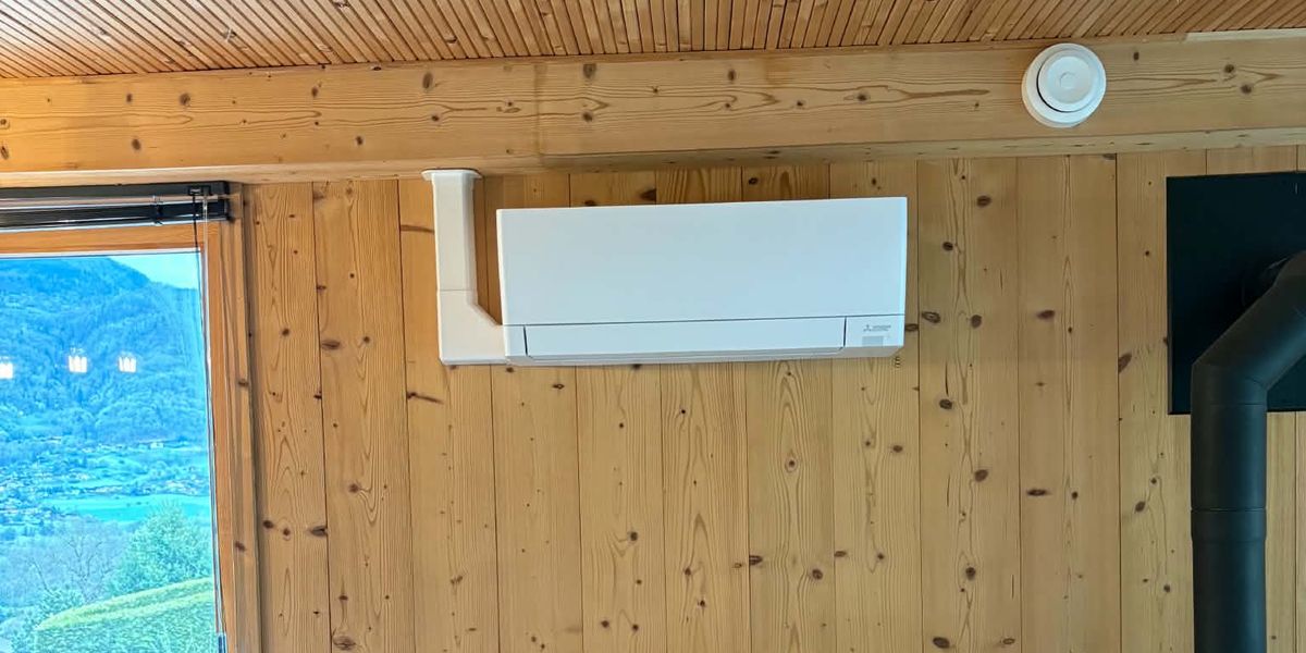 Climatiseur mural Mitsubishi Electric posé sur un lambris bois, à côté d’une fenêtre
