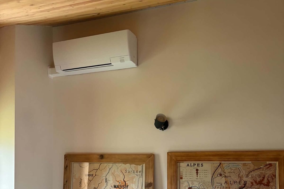 Climatiseur mural posé sous un plafond bois, au-dessus de deux cartes anciennes encadrées