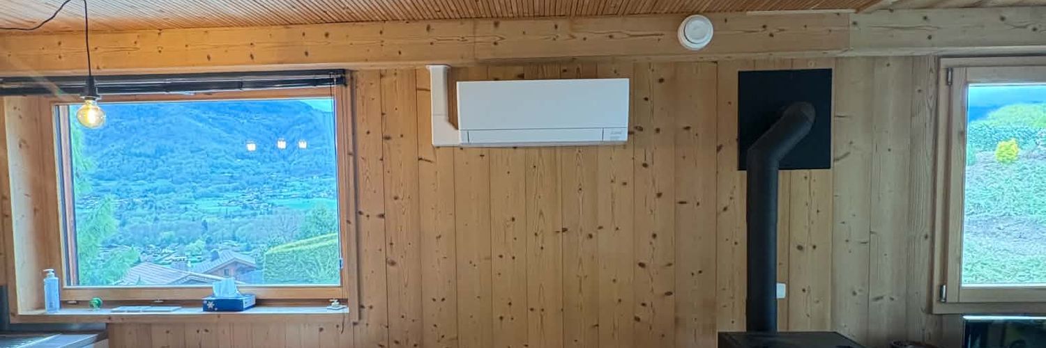 Séjour en bois : climatiseur mural entre la fenêtre et le conduit du poêle