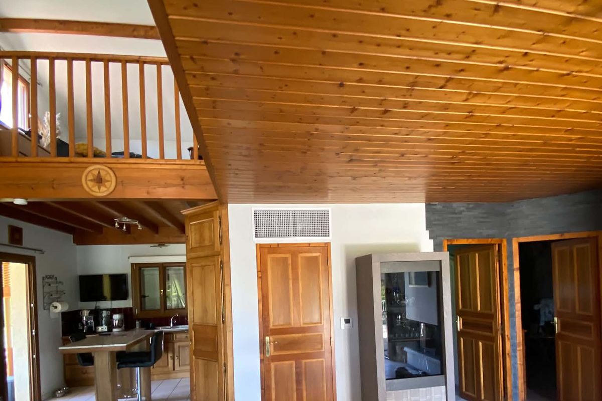 Grande pièce sous plafond bois : la grille de soufflage du gainable s’intègre au-dessus d’une porte