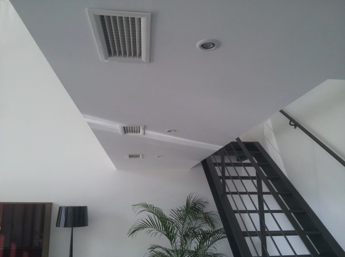 Grilles de soufflage du gainable intégrées au plafond d’un séjour, au-dessus d’un escalier métallique