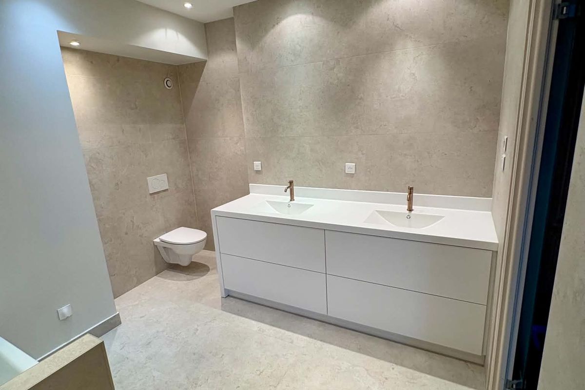 Salle de bain rénovée : meuble double vasque blanc, robinetterie cuivrée et WC suspendu
