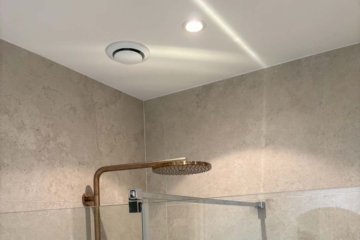 Bouche d’extraction ronde au plafond d’une salle de bain, au-dessus d’une douche à colonne cuivrée